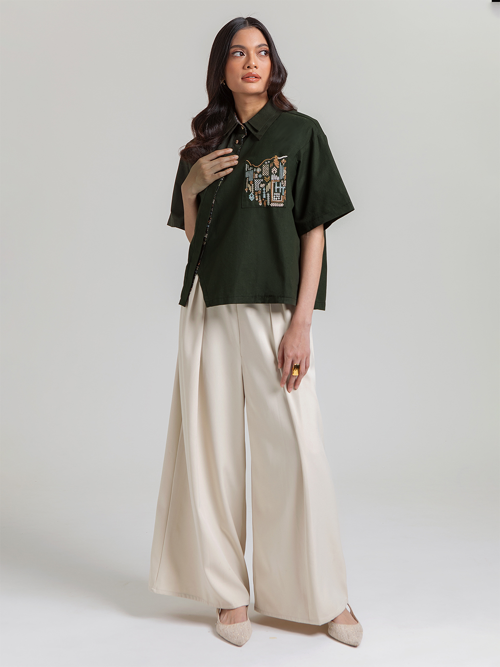 DISKON 15%. Atasan wanita kemeja lengan pendek premium dari bahan textured cotton yang adem dan busui-friendly. Desain asimetris modis dengan detail bordir saku artistik.