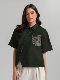 DISKON 15%. Atasan wanita kemeja lengan pendek premium dari bahan textured cotton yang adem dan busui-friendly. Desain asimetris modis dengan detail bordir saku artistik.
