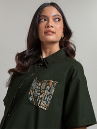 DISKON 15%. Atasan wanita kemeja lengan pendek premium dari bahan textured cotton yang adem dan busui-friendly. Desain asimetris modis dengan detail bordir saku artistik.